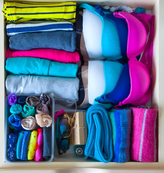 Neatly folded clothes with accessories in chest of drawers - Фото, изображение