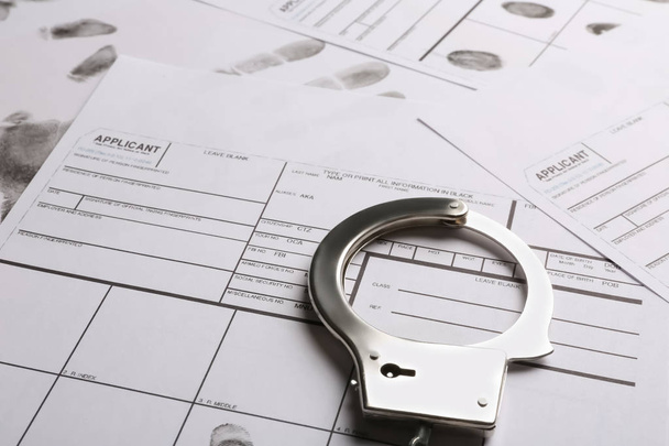 Handcuffs and fingerprint record sheets, closeup. Criminal investigation - Foto, Imagen