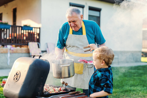 grandfather carefully teaching adorable boy to grill - Foto, Imagen
