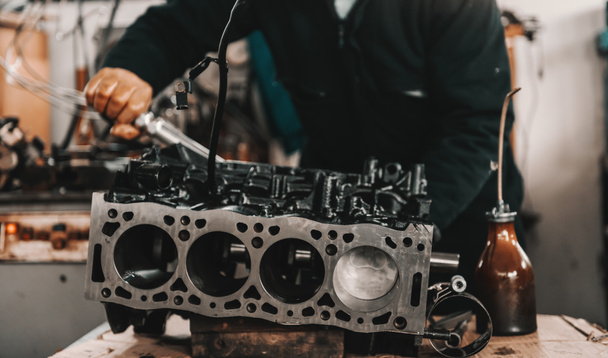 Auto mechanic adjusting cylinder head on engine block with wrench at workshop. - Photo, Image