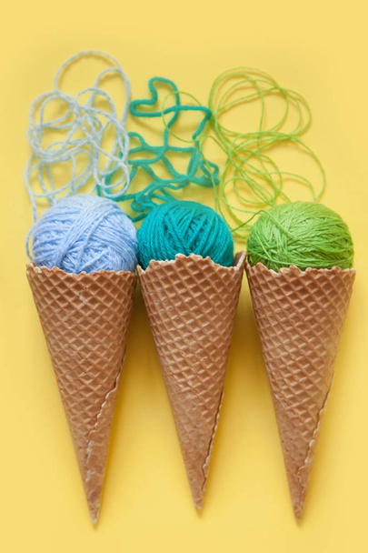 Balls of yarn lie in a waffle cone for ice cream. Coloured wool. - Foto, Imagen