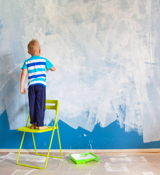 The child paints the blue wall with a roller. The boy holds a la - Photo, Image
