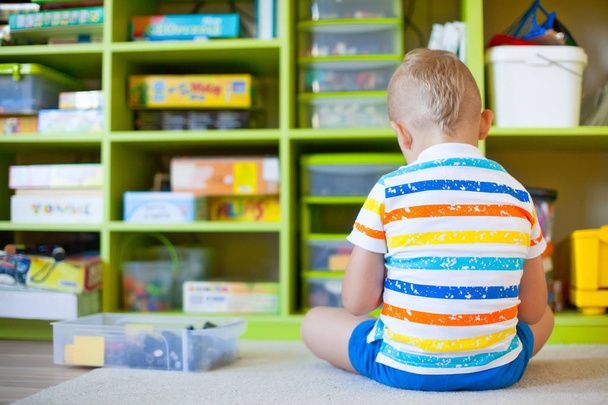 Petit garçon blond jouant avec beaucoup de blocs en plastique coloré à l'intérieur. De nombreux jeux de société
. - Photo, image