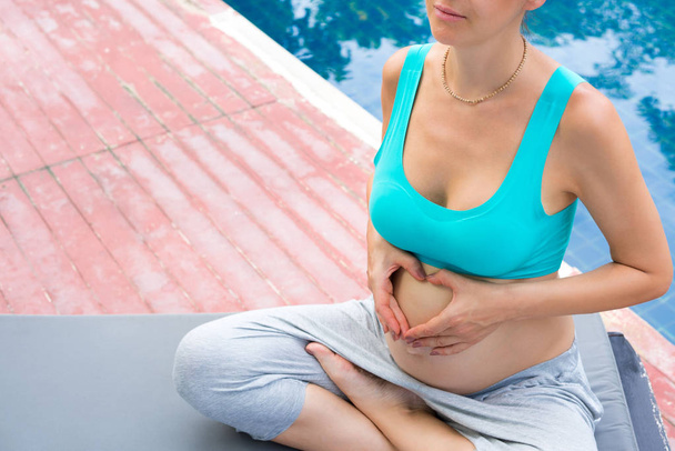 Μια έγκυος γυναίκα κάθεται σε στάση λωτού. Γιόγκα στην αυλή - Φωτογραφία, εικόνα