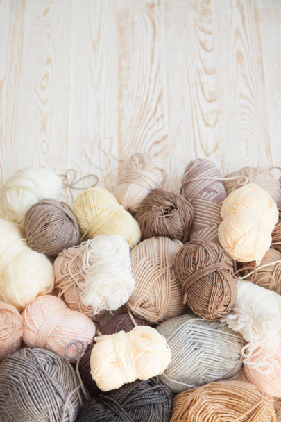 The yarn is beige, brown, gray and white. The background is aged wood. Knitting needles, scissors, coffee, knitting, knitted fabric. - Foto, Imagen