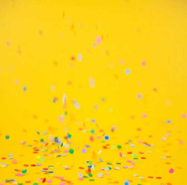 Colored confetti flying on yellow background - Foto, Imagen