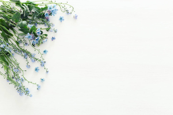 boeket van blauw en delicate blauwe bloemen beschermveren over witte houten achtergrond. bovenaanzicht, plat lag - Foto, afbeelding