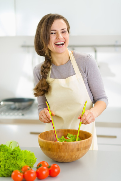 Smiling young woman mixing fresh salad - Foto, afbeelding