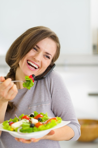 サラダを食べると携帯電話を話している若い女性の笑みを浮かべてください。 - 写真・画像
