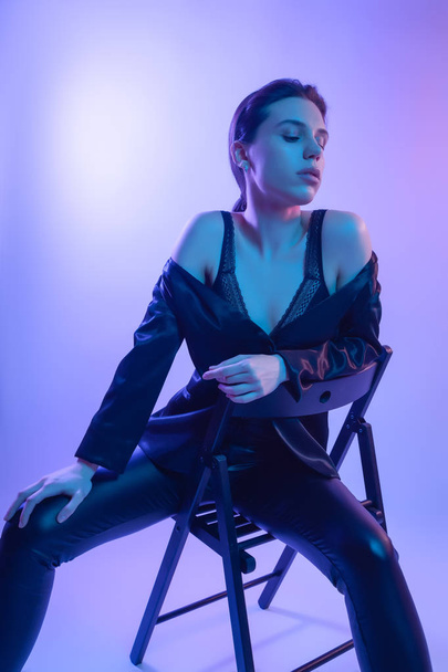 Cinematic night portrait of woman in  neon. High Fashion model girl in colorful bright neon lights posing on chair in studio, portrait of beautiful woman in   jacket, underwear and trousers.  - Foto, immagini