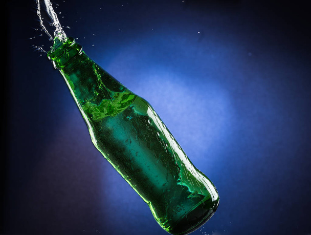 Falling and jumping green bottle with spilling liquid on a blue gradient background - Valokuva, kuva