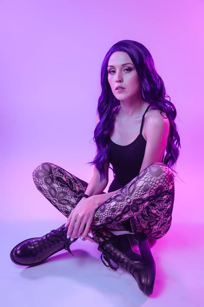 Beautiful woman with long purple hair in black underwear, pantyhose posing in attractive position in colorful bright neon blue and pink lights in studio. Fashion concept - Valokuva, kuva