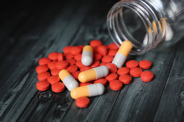 Pullo hajallaan pillereitä ja kapseleita tumma puinen pöytä. Lääkkeiden, antibioottien, vitamiinien, apteekkien, kylmän ja flunssan hoidon käsite
 - Valokuva, kuva