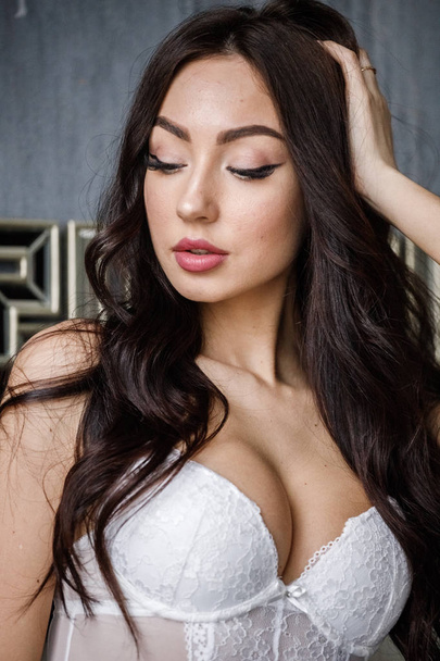 Studio portrait of beautiful brunette woman wearing white lingerie. Charming beauty model posing at apartments interior   - 写真・画像