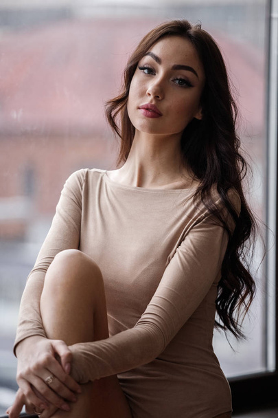 Studio portrait of beautiful brunette woman wearing beige clothes. Charming beauty model posing at apartments interior   - Фото, изображение