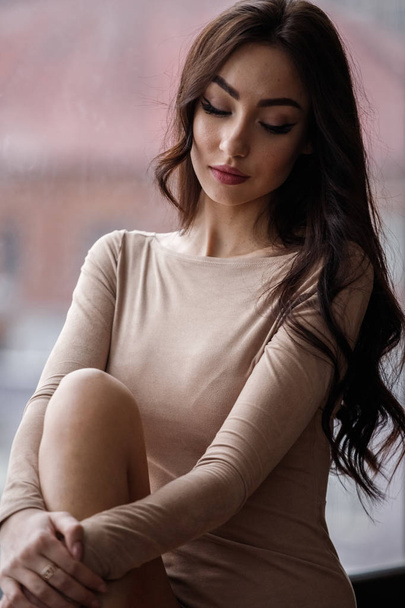 Studio portrait of beautiful brunette woman wearing beige clothes. Charming beauty model posing at apartments interior   - Foto, Imagen