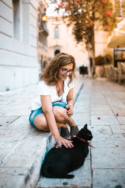 Kadın sokakta bir kedi ile oynarken - Fotoğraf, Görsel