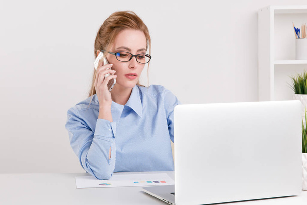 Sérieuse jolie femme blonde travaillant au bureau par son nboteboo et parlant son téléphone
. - Photo, image