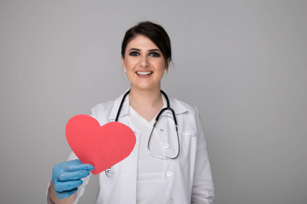 Woman in a white coat with stethoscope around neck holding image of heart. - Photo, Image