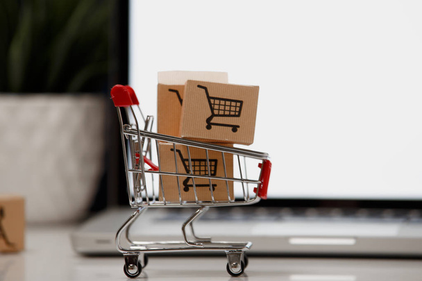 Many paper boxes in a small shopping cart on a laptop keyboard. Concepts about online shopping that consumers can buy things directly from their home or office just using a few clicks via web browser. - 写真・画像