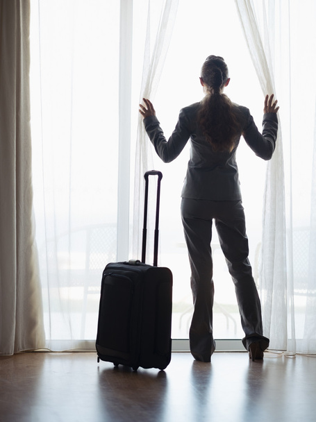 Silhouette of business woman with wheel bag looking into hotel window - Foto, Imagem