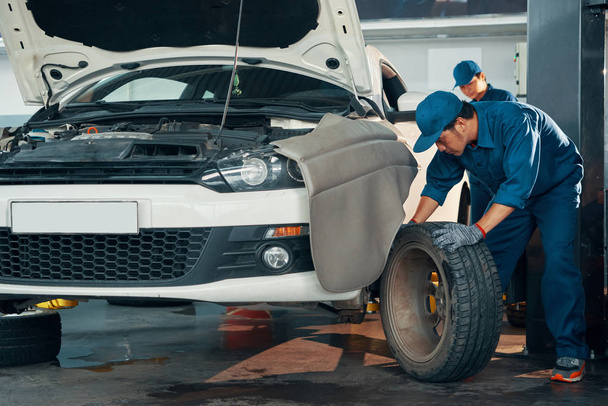 auto service werkplaats garage, mechanic werknemers repareren wiel van de auto  - Foto, afbeelding