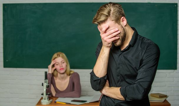 He left a lesson unlearned. University or college student covering face. Male student with examiner at examination. Handsome man standing in classroom with teacher. High school student saying lesson - Foto, imagen