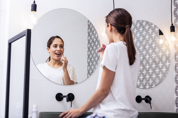 Appealing woman brushing teeth in front of circular mirror - Photo, image