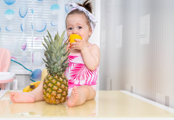 Baby girl on table with pineapple and lemon - Фото, зображення
