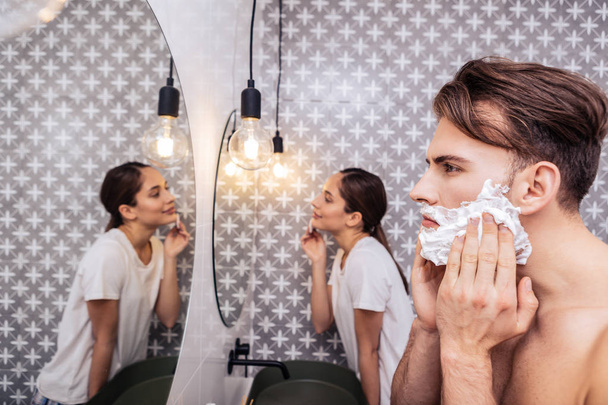 Dark-haired husband shaving his face standing near appealing wife - Valokuva, kuva