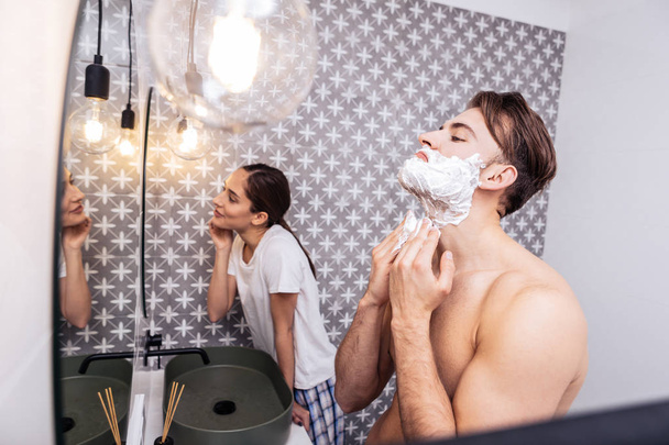 Strong sexy husband shaving his face standing near his woman - Foto, Imagen