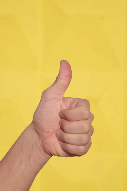 Close-up van mannenhand duimen omhoog teken tegen een gele achtergrond weergeven. - Foto, afbeelding
