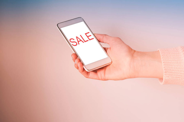 Hand with mobile phone screen on pink. Word sale - Photo, image