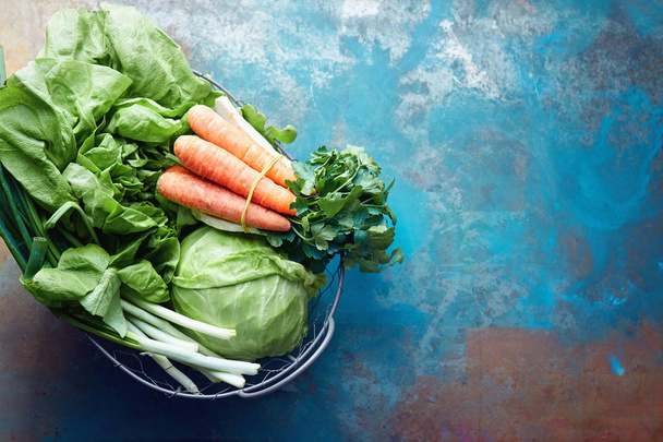 Fresh lettuce, cabbage, spring onions, carrots and parsley in a wire basket on a table.  - Photo, image