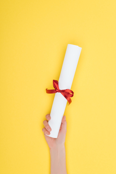 Cropped view of woman holding diploma with ribbon on yellow surface - Fotoğraf, Görsel