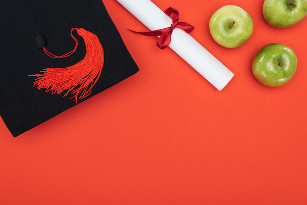Bovenaanzicht van academische GLB, diploma en appels op rode oppervlak - Foto, afbeelding