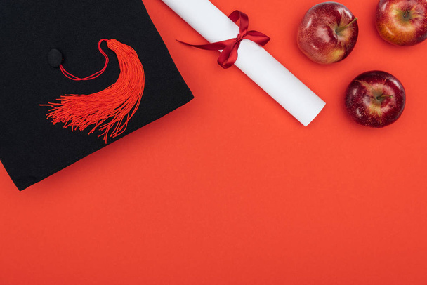 Top view of academic cap, diploma and apples on red surface - Valokuva, kuva