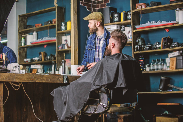 Hipster client got new haircut. Barber finished trimming. Barber with bearded man looking at mirror, barbershop background. Haircut concept. Client and professional master checking result - Photo, Image