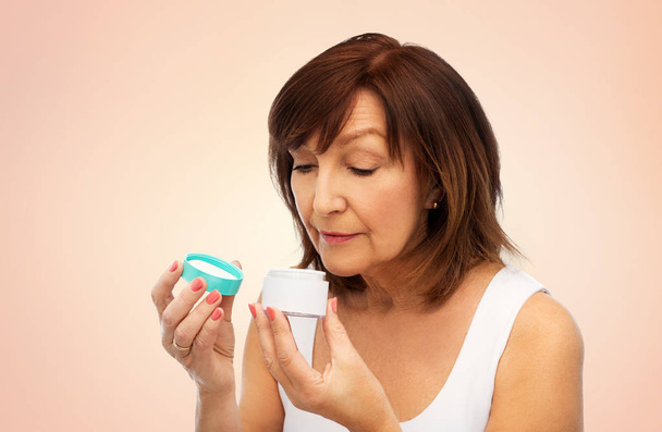 senior woman with cream jar over beige background - Photo, Image