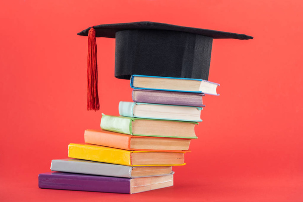 Akademické čepice se střapcem a světlé knihy na červené ploše - Fotografie, Obrázek