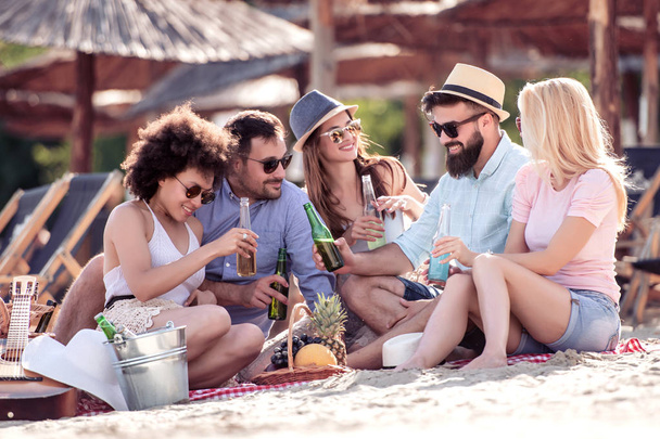 Vrienden genieten van een goed humeur en de picknick op het strand. Lifestyle, liefde, dating en vakantie concept. - Foto, afbeelding