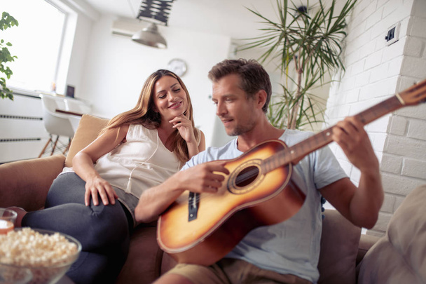 Usmívající se pár těší doma, muž hraje na kytaru. - Fotografie, Obrázek