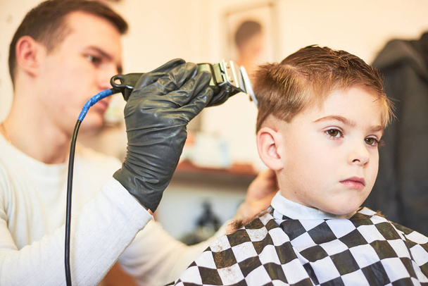 Partial image of male barber making haircut of little boy at salon - Фото, изображение