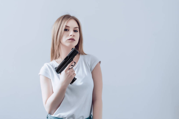 Krásná mladá dívka drží zbraň v ruce. Pistole, zvýšit až na obličej. - Fotografie, Obrázek