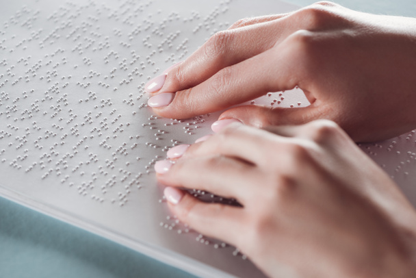 bijgesneden weergave van meisje lezen van braille tekst met handen op wit papier - Foto, afbeelding