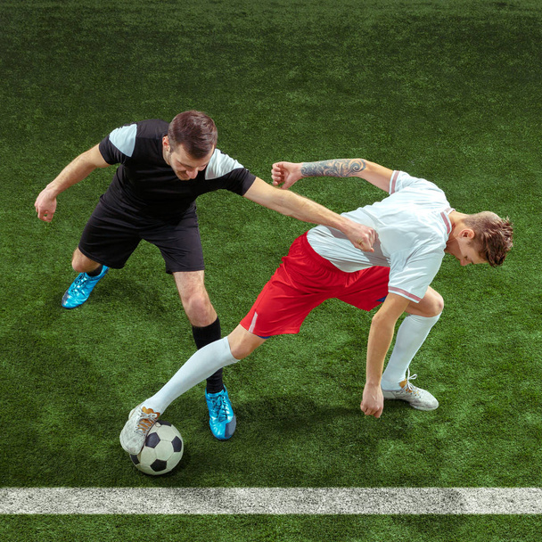 Football players tackling ball over green grass background - Valokuva, kuva
