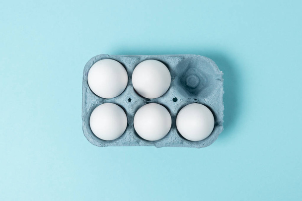 Easter white eggs in carton tray on blue background. Flat lay. Minimal concept. - Foto, afbeelding