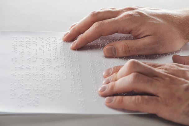 cropped view of man reading braille text with hands isolated on grey - Foto, Imagen