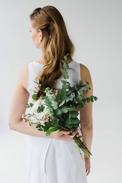 back view of girl in elegant dress holding flowers behind back isolated on white - Foto, Bild