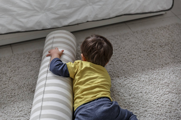 Un ragazzo biondo carino gioca e si diverte sul tappeto nella sua camera da letto
 - Foto, immagini